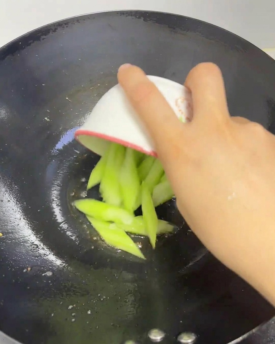 Fette di luffa verde fresca aggiunte da una ciotolina in un wok riscaldato.