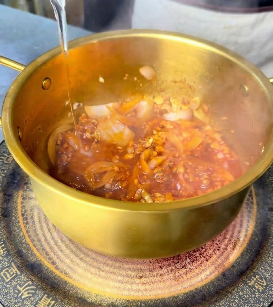 Acqua fresca versata in una pentola di ottone che si mescola alla base piccante rossa.