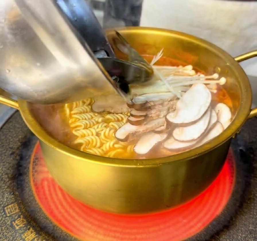 Gamberi e cozze freschi versati da una ciotola dacciaio nella pentola dorata con noodle e funghi.