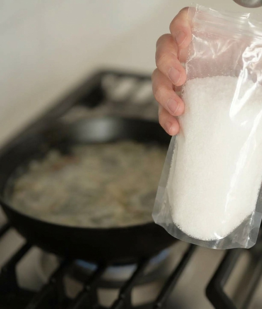 Una mano versa del condimento in polvere chiaro in una padella con il brodo che sobbolle.