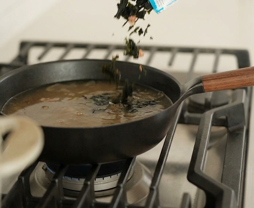 Pezzetti di alga essiccata versati direttamente in una padella con brodo scuro fumante.