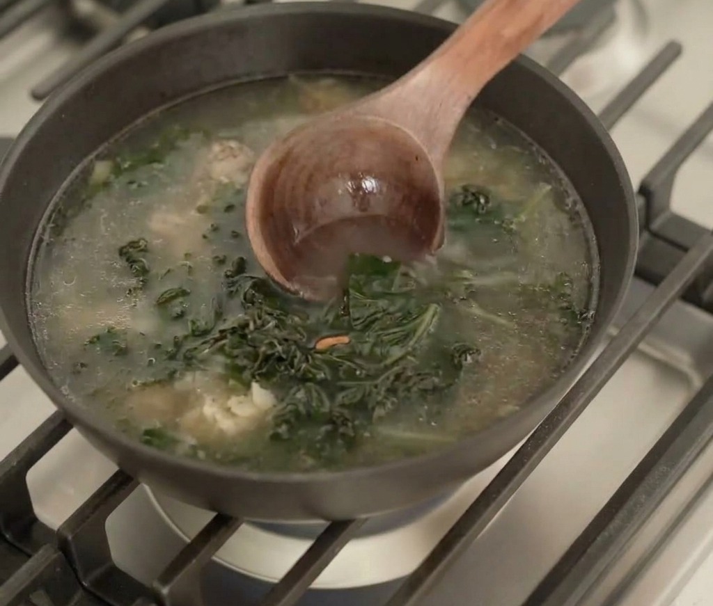 Un mestolo di legno mescola il brodo con lalga reidratata in una padella nera sul fuoco.