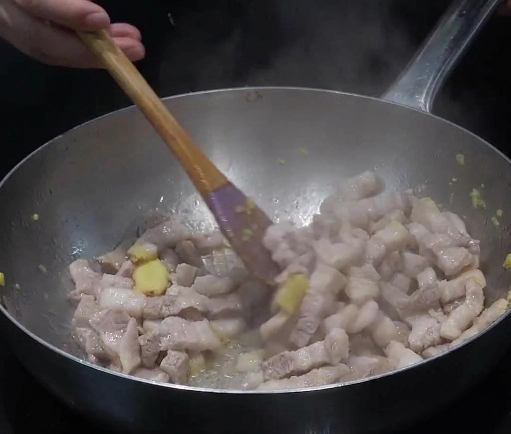 Fette di pancetta e zenzero tritato saltati in una grande padella dacciaio inox con vapore che sale.