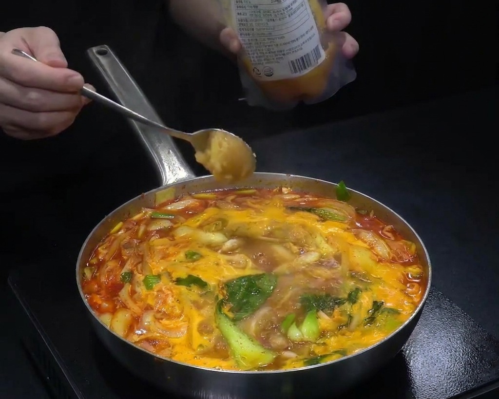 Un cucchiaio di aglio tritato aggiunto a una padella di zuppa rossa bollente piena di cavolo e cipolle.