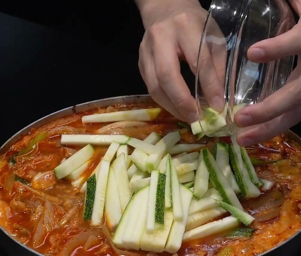 Zucchine a fette e peperoncini verdi tritati aggiunti sopra una pentola di zuppa di pesce rossa.