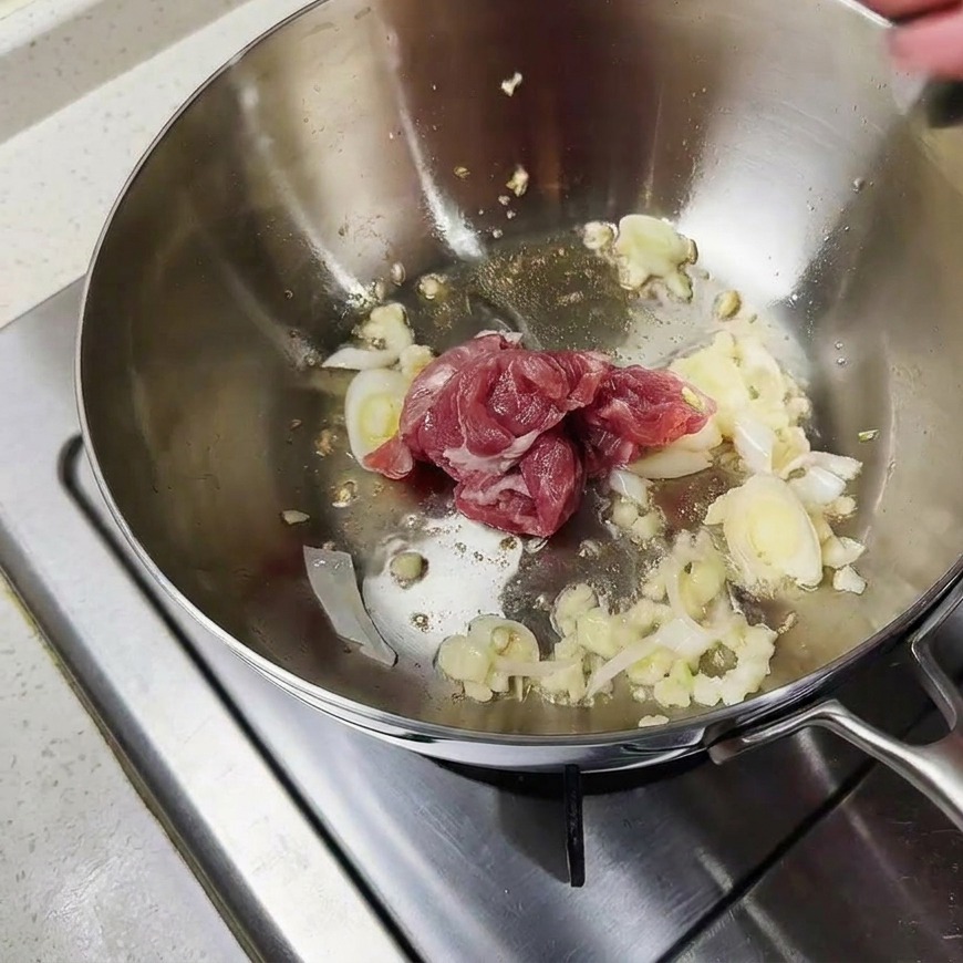 Pezzetti di maiale crudo saltati con gli aromi sul fondo di una pentola di metallo.