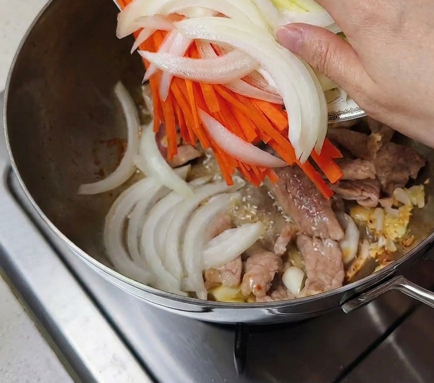 Cipolle affettate, carote e zucchine aggiunte nella pentola con la carne.