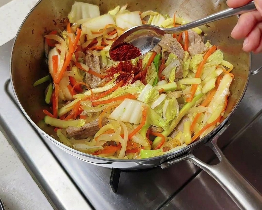 Peperoncino coreano rosso in polvere versato sulle verdure saltate nella pentola.