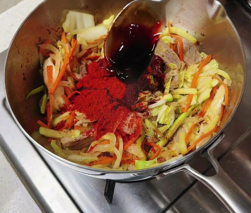 Salsa di soia versata sulle verdure e il peperoncino in una pentola dacciaio.