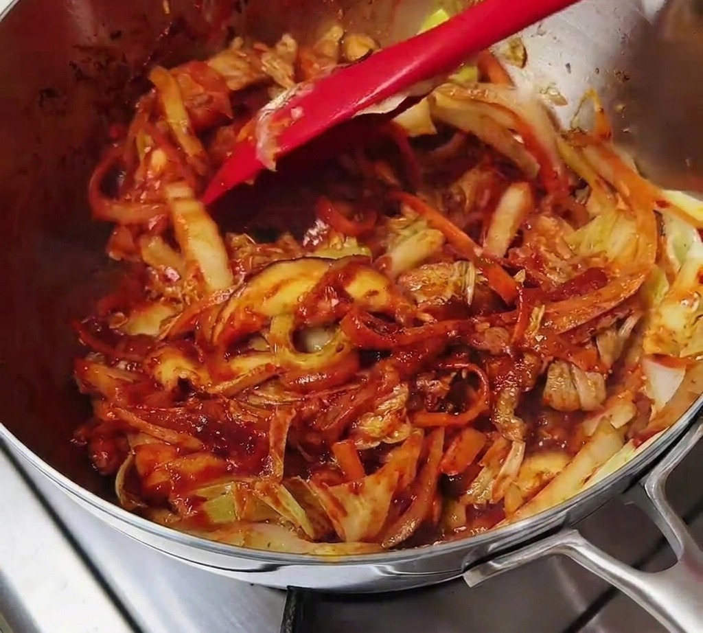Spatola che mescola carne e verdure completamente avvolte da un condimento rosso intenso.