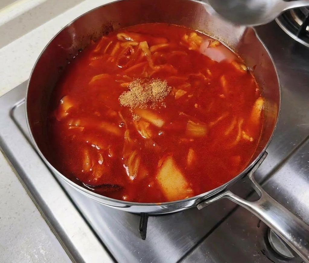 Brodo granulare di manzo aggiunto al centro di una zuppa rossa che sobbolle.