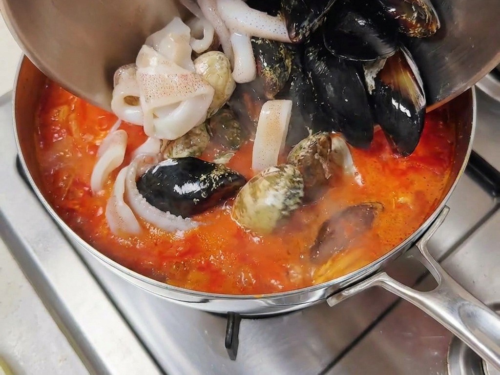 Misto di cozze e anelli di totano versati da una ciotola nel brodo rosso bollente.