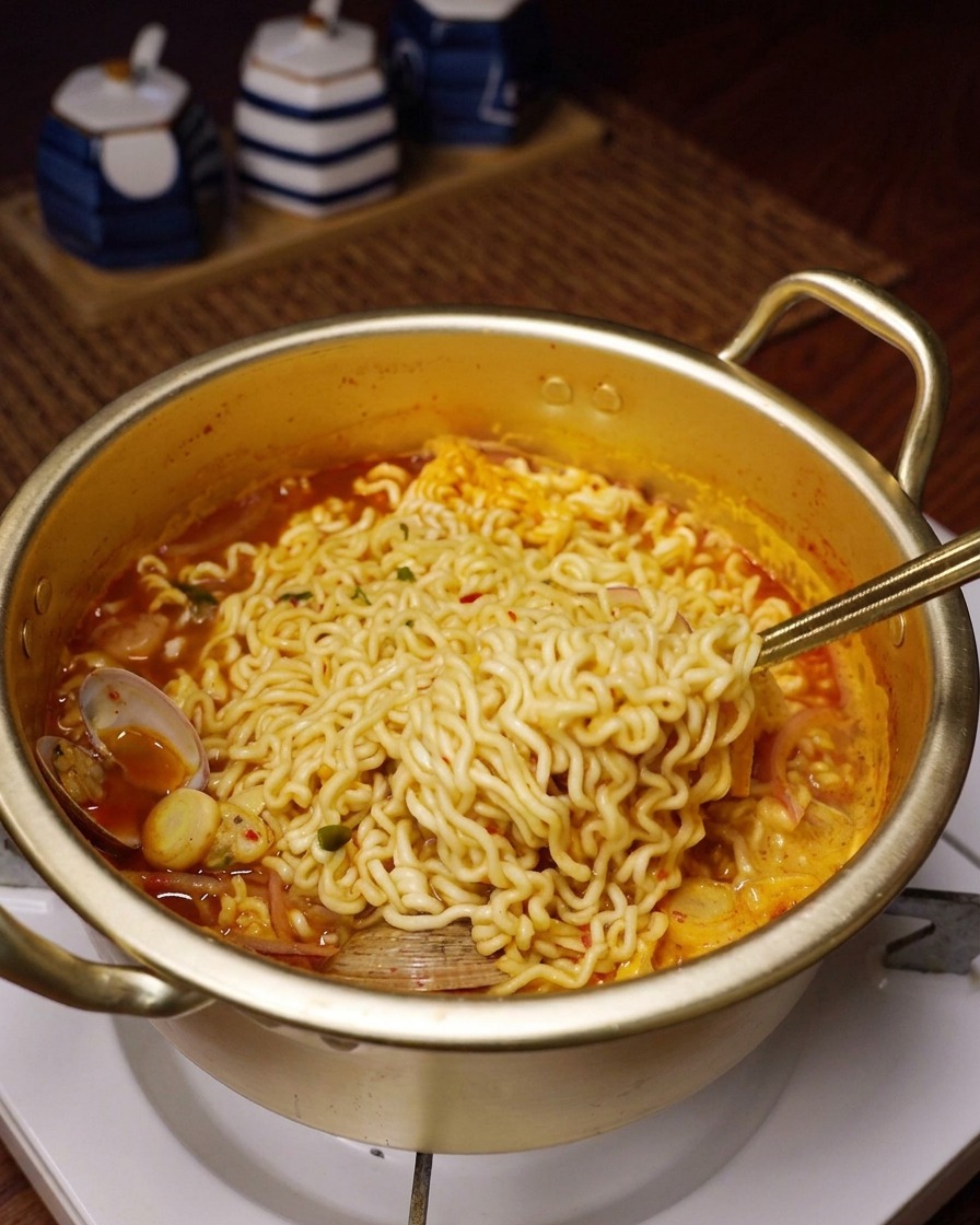 Noodles istantanei sollevati dal brodo rosso con un cucchiaio di metallo.