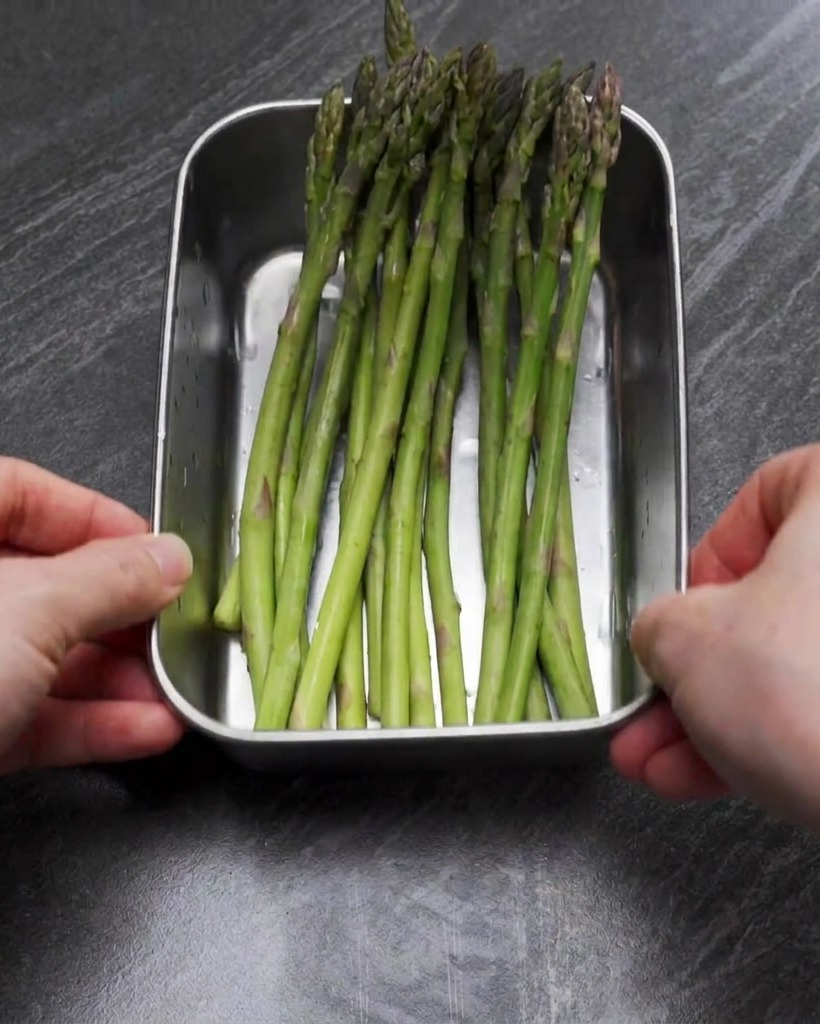 Un vassoio in acciaio inossidabile pieno di asparagi verdi brillanti tagliati a pezzetti.