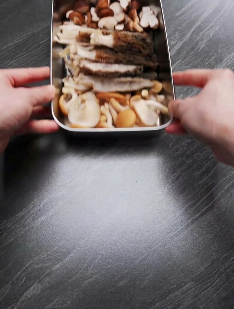 Mani che tengono un vassoio di metallo contenente un mix di spugnole affettate e funghi shiitake tagliati a metà.