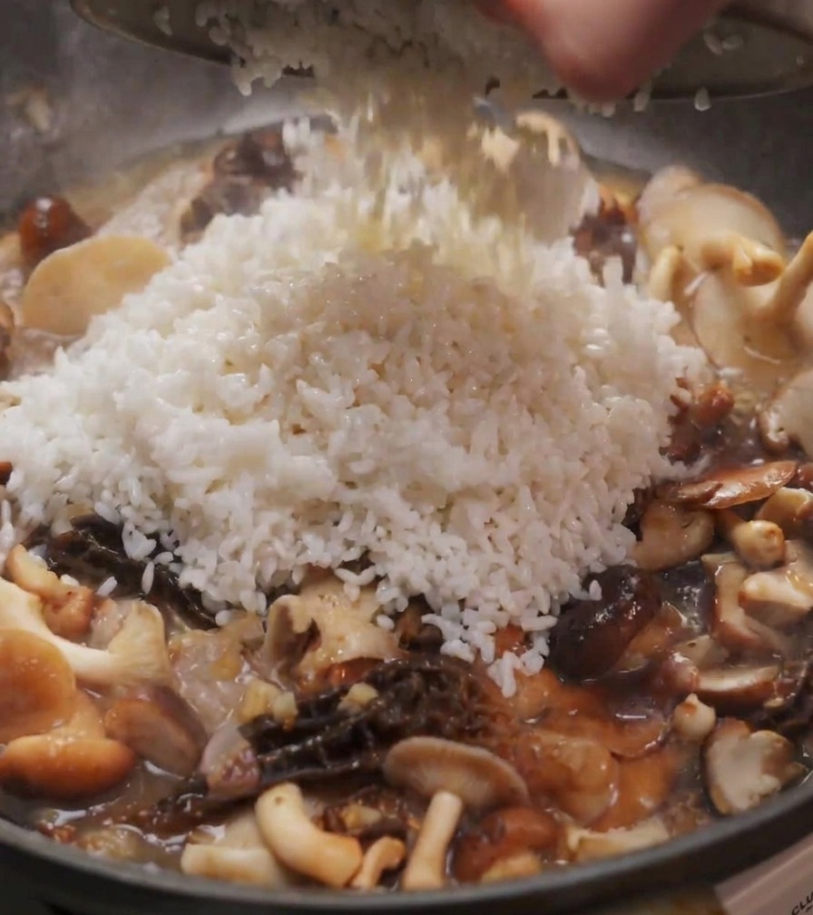 Un mucchio di riso bianco versato da una ciotola in una padella piena di funghi shiitake e spugnole saltati.