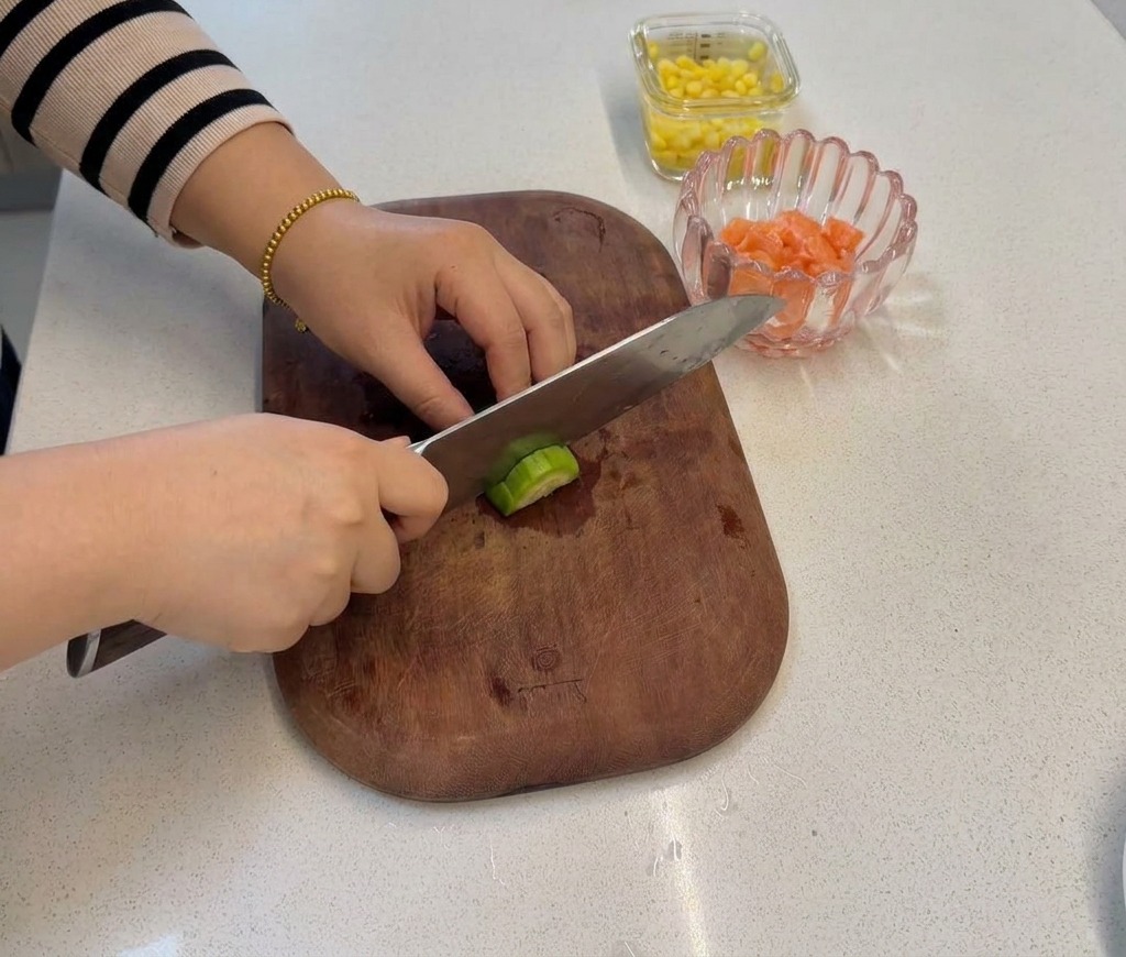 Una mano che taglia con un coltello il gambo di un broccolo su un tagliere, creando piccole cimette della dimensione di un boccone.
