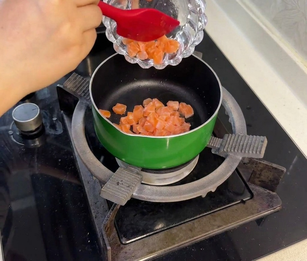 Cubetti di salmone crudo marinato aggiunti in una piccola padella verde e saltati in padella finché lesterno non diventa opaco e rosa chiaro.
