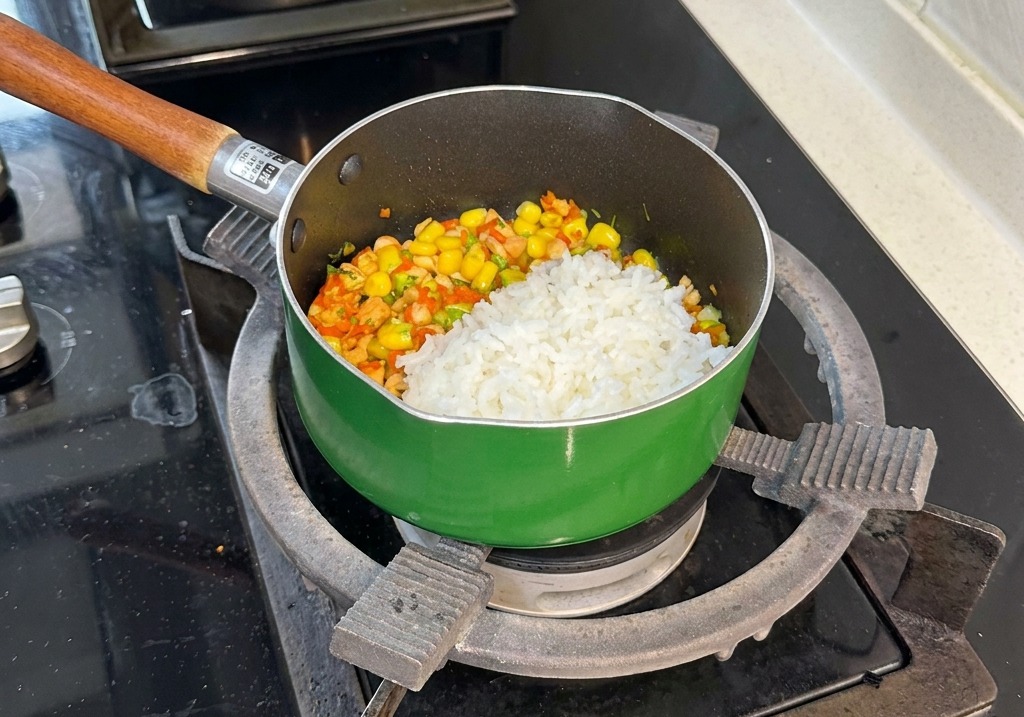 Un mestolo di riso bianco cotto al vapore posizionato sopra il colorato mix di salmone, mais, carote e broccoli nella padella.