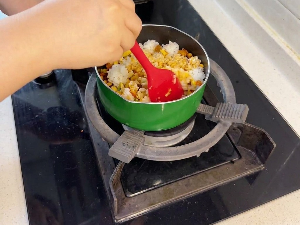 Una persona usa una spatola rossa per mescolare il riso bianco con il salmone e le verdure in una padella verde sui fornelli.