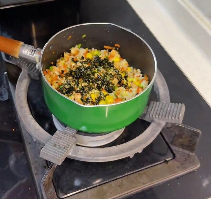 Fiocchi di alghe scure cosparsi da un piccolo barattolo di vetro su una padella di riso, salmone e verdure appena mescolati.