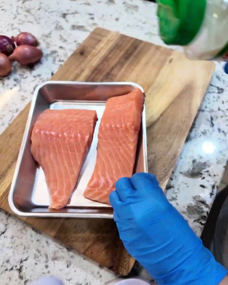 Filetti di salmone crudo conditi con aglio in polvere e pepe nero in una teglia di metallo.