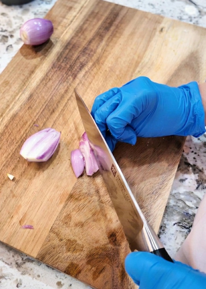 Un coltello da cucina che taglia a rondelle sottili degli scalogni viola su un tagliere di legno.