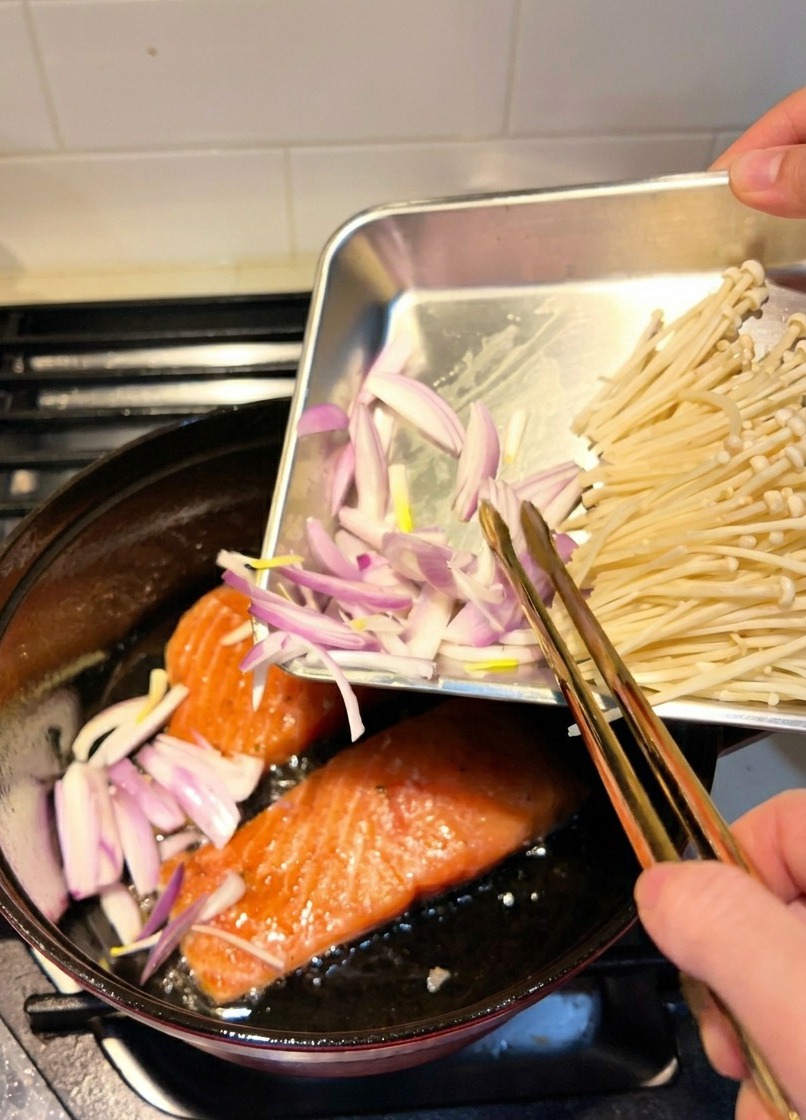 Scalogni affettati aggiunti in una pentola dove i filetti di salmone stanno rosolando nellolio.