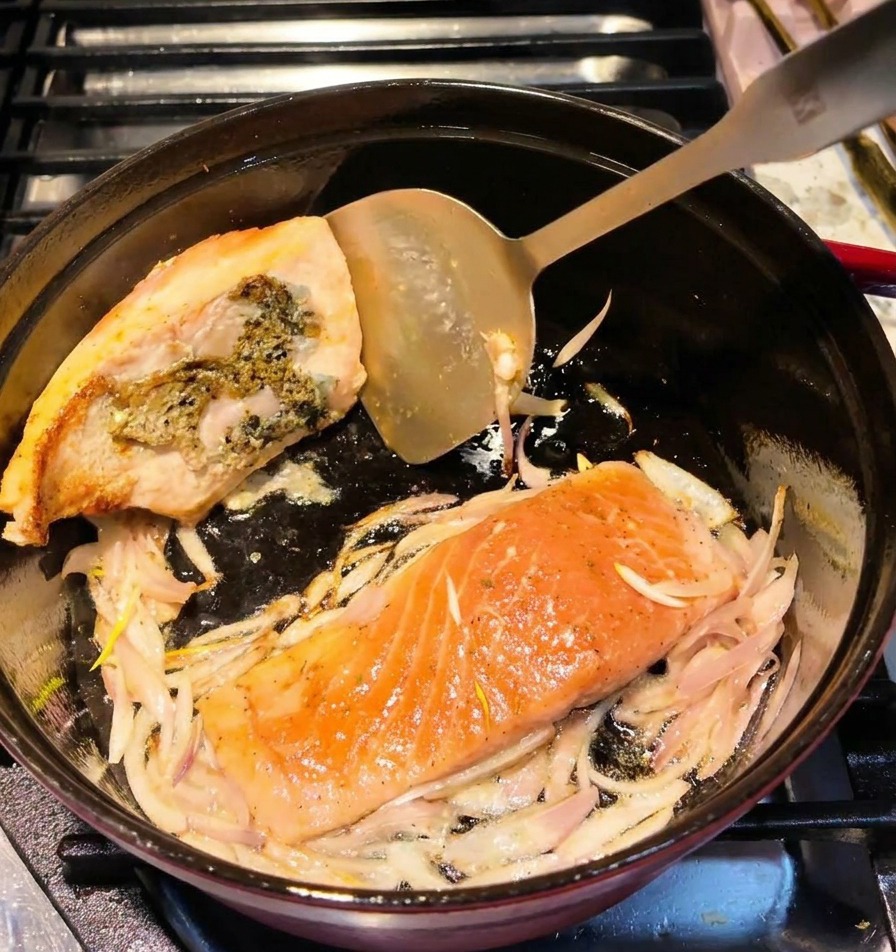 Una spatola di metallo gira un filetto di salmone nella pentola, mostrando la crosticina dorata.