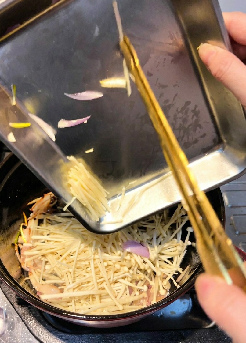 I funghi enoki vengono aggiunti nella pentola per essere saltati insieme agli scalogni.