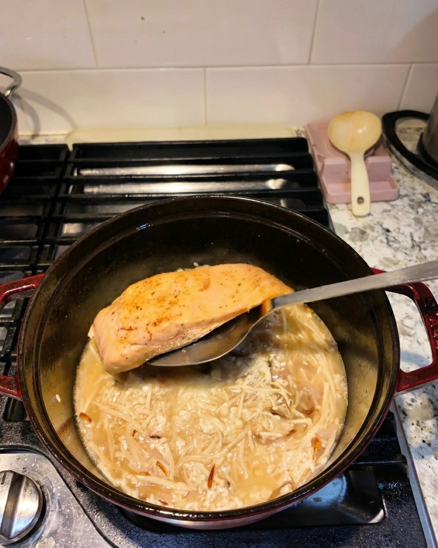 Una spatola di metallo posiziona un filetto di salmone scottato nella pentola, sul letto di riso, funghi enoki e acqua.