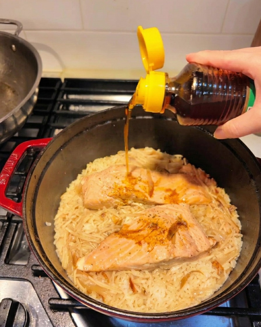 Olio di sesamo tostato versato da una bottiglia dal tappo giallo sopra il riso e il salmone finiti.