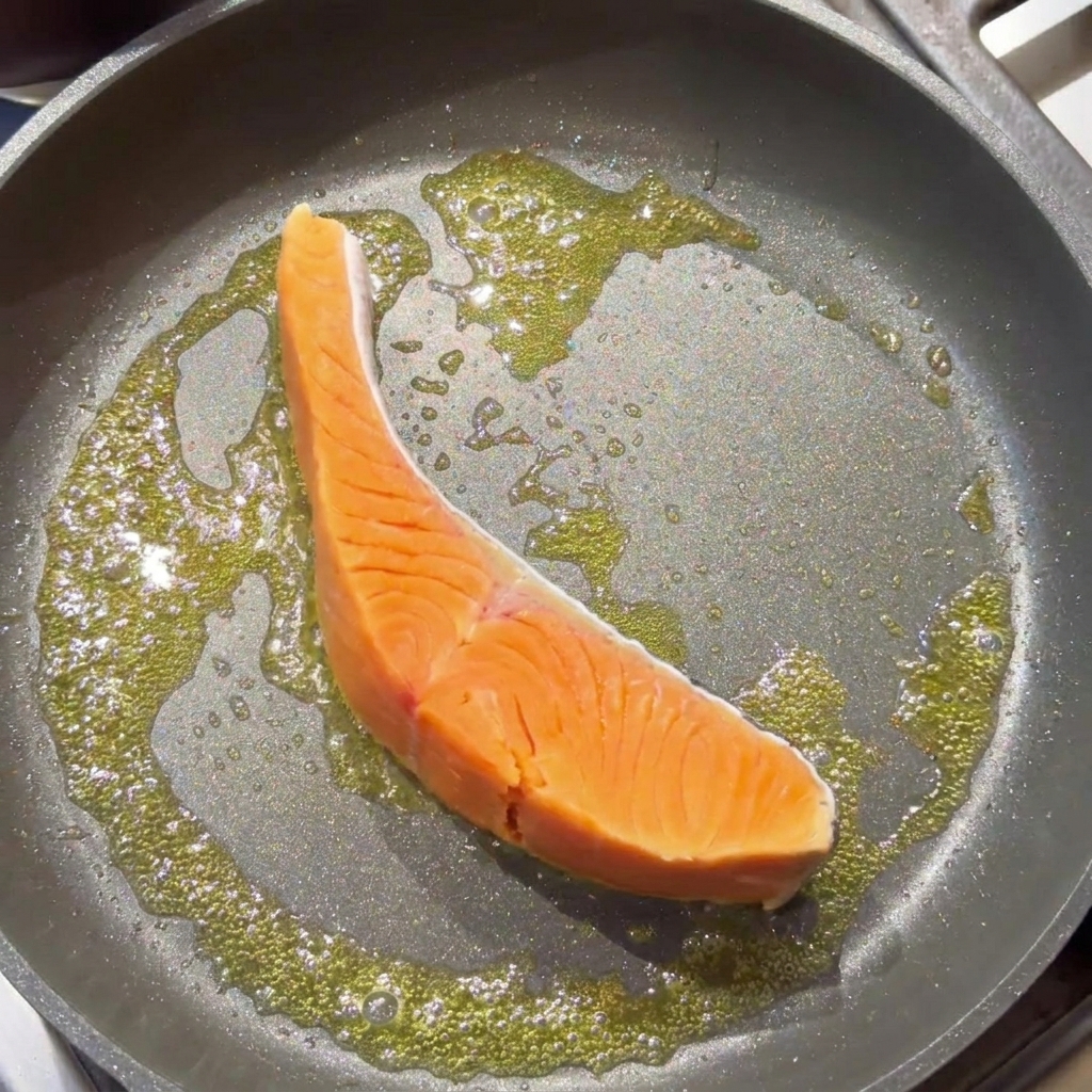 Un filetto di salmone crudo che sfrigola in padella con burro fuso.