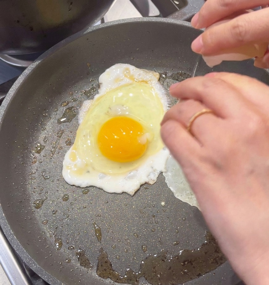 Un uovo appena rotto in una padella antiaderente per essere strapazzato.