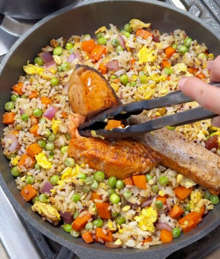 Pinze da cucina che tengono un pezzo di salmone scottato sopra il riso saltato.