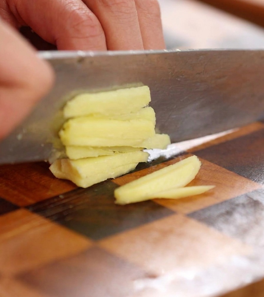 Primo piano di un coltello che trita finemente una fetta di zenzero fresco su un tagliere.