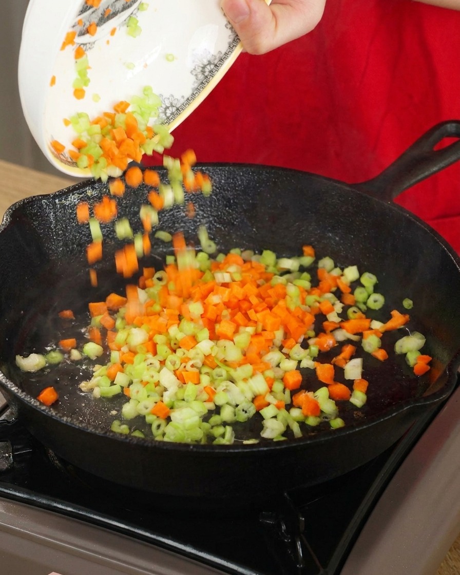 Cubetti di carote e sedano versati da una ciotola in una padella di ghisa calda per essere saltati.
