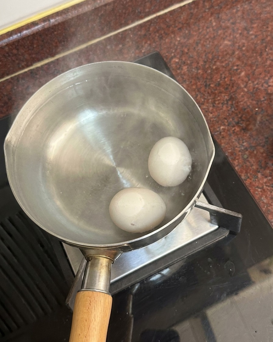 Due uova bianche sul fondo di una pentola piena dacqua calda, con il vapore che sale in superficie.