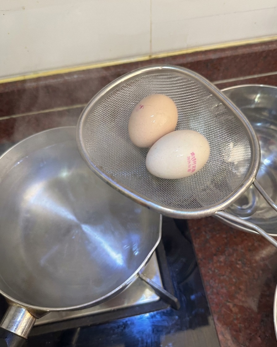 Un colino con due uova cotte sopra una pentola dacqua, pronte per essere messe in una ciotola con acqua e ghiaccio.