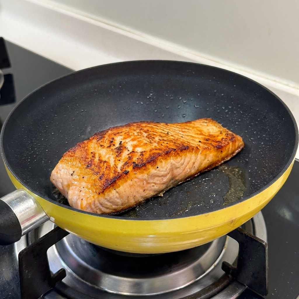 Filetto di salmone scottato in una padella gialla che mostra una superficie dorata e croccante.
