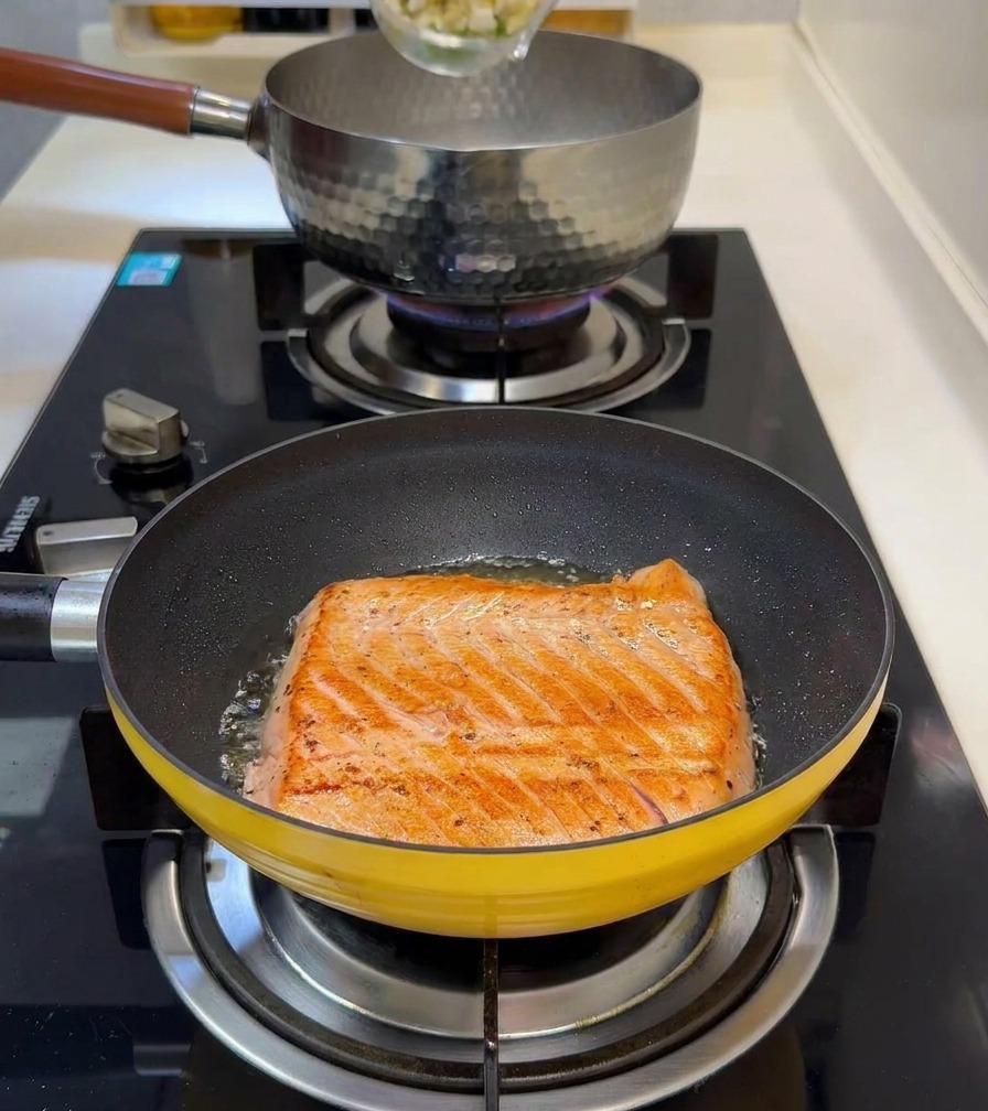 Germogli di bambù a dadini e piselli versati in un pentolino dacqua bollente con il salmone che scotta in primo piano.