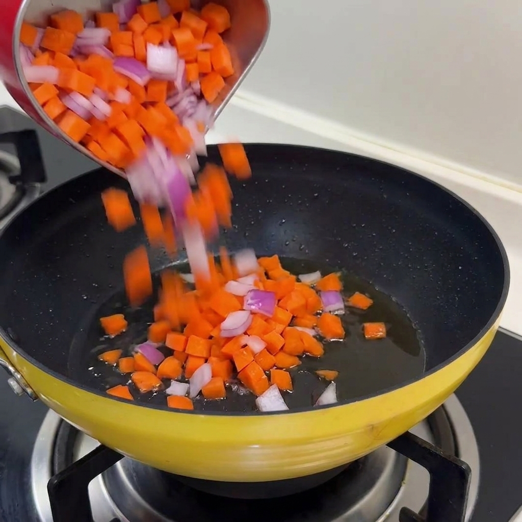 Mix di carote a dadini e cipolle rosse versate in una padella gialla con olio caldo.