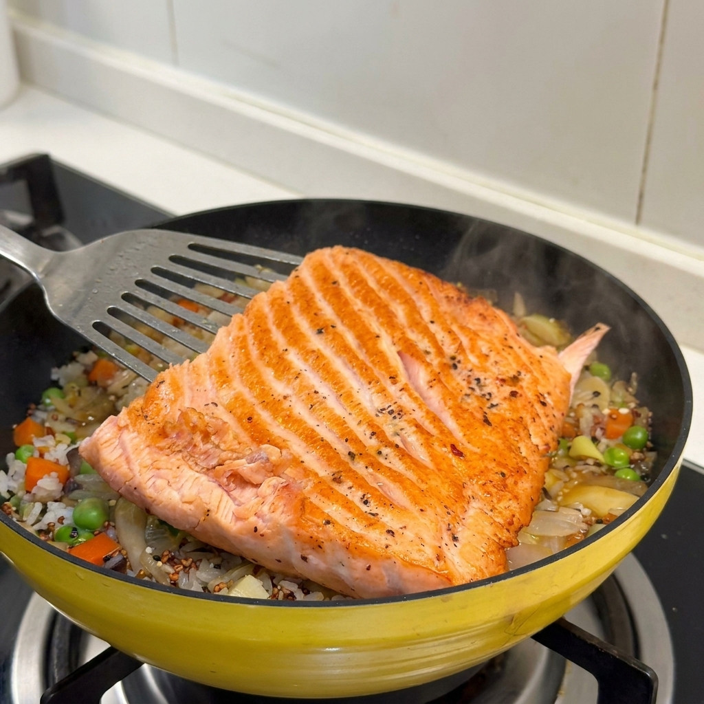 Un grande filetto di salmone dorato viene posizionato sopra il letto di riso e verdure in padella.