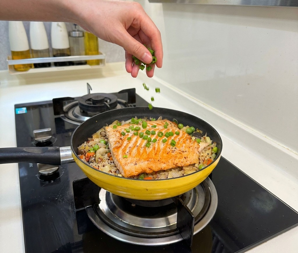 Una mano spolvera cipollotti verdi tritati sopra il piatto finito di riso e salmone.