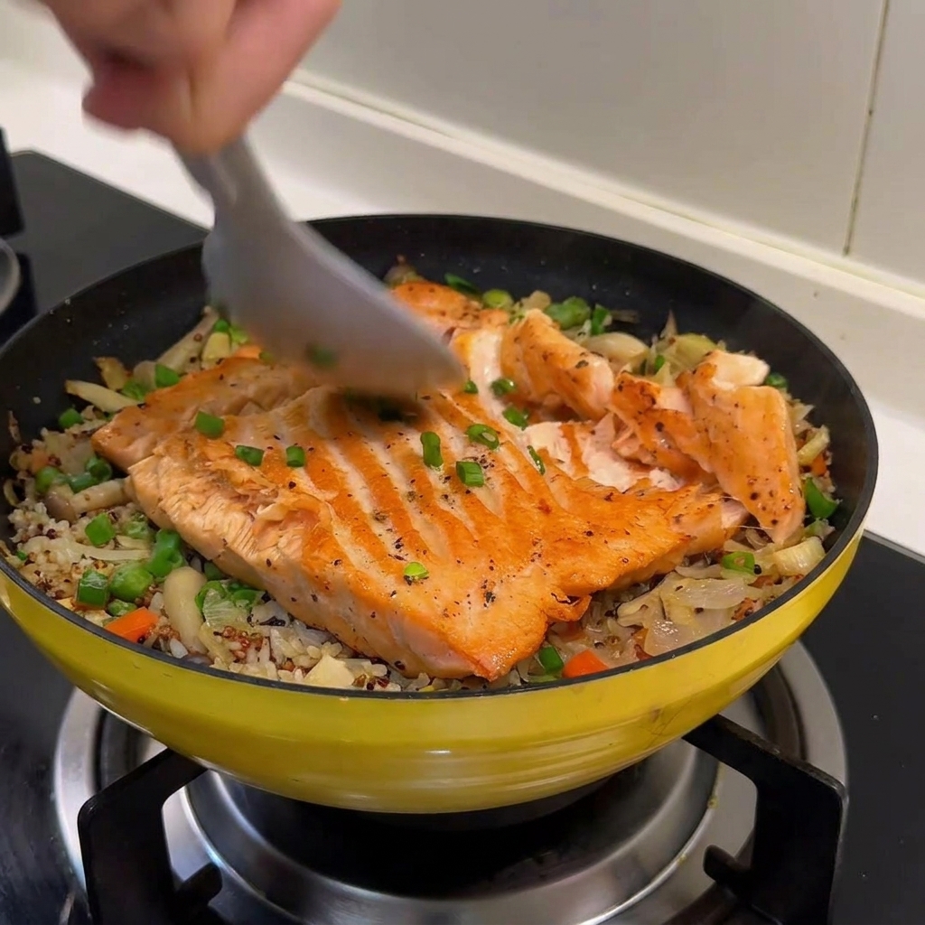 Un cucchiaio di metallo rompe il filetto di salmone cotto in fiocchi sopra il letto di riso e verdure.