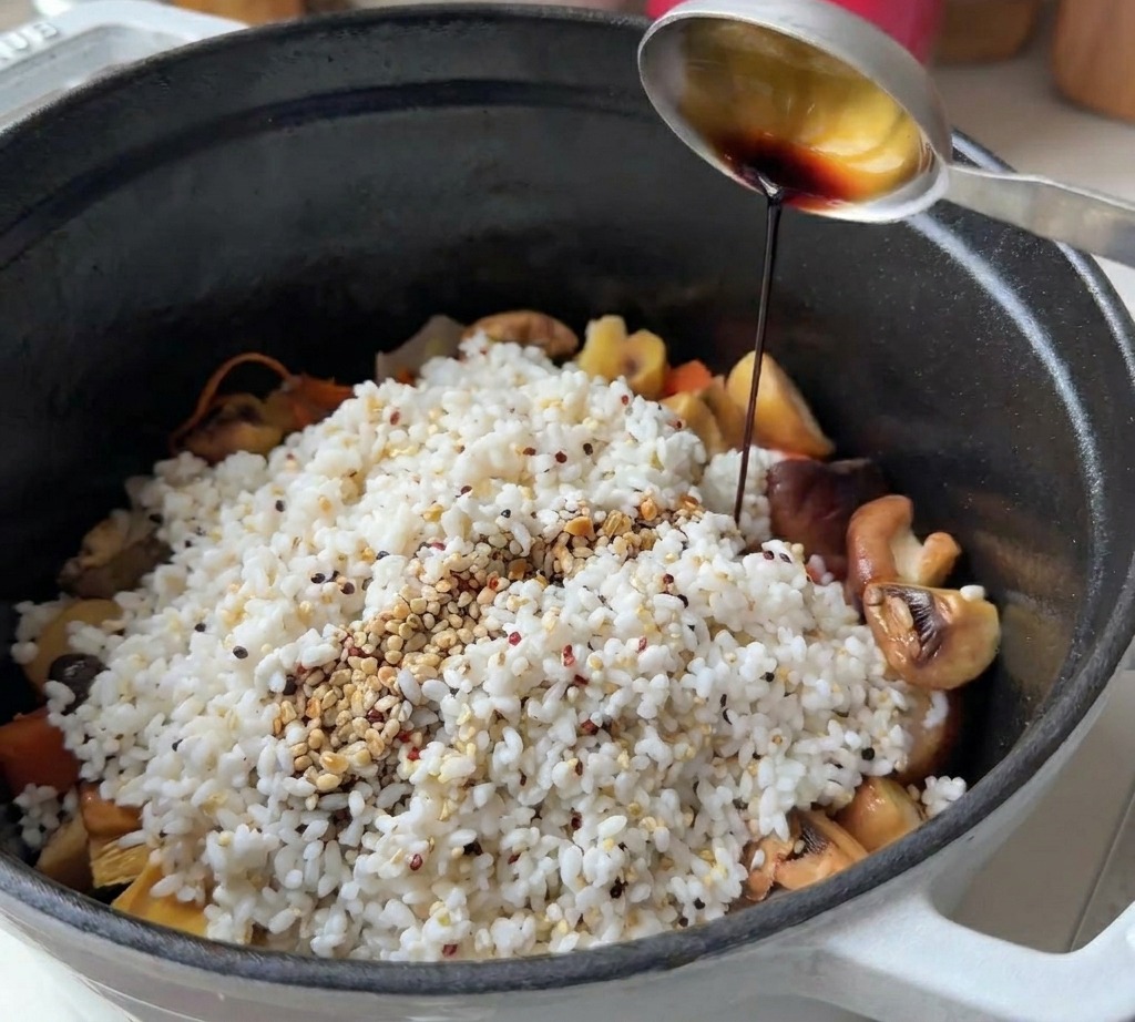 Cucchiaio di metallo che versa salsa di soia su riso e quinoa in una pentola nera.