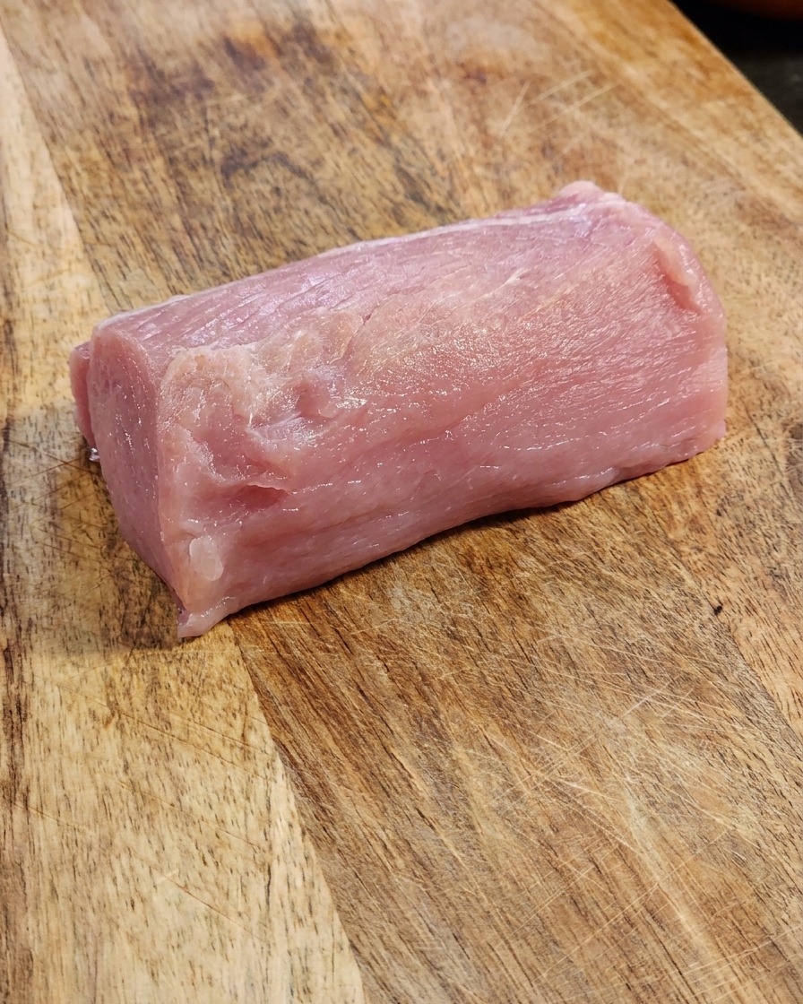 Fetta spessa di lombo di maiale crudo su un tagliere di legno