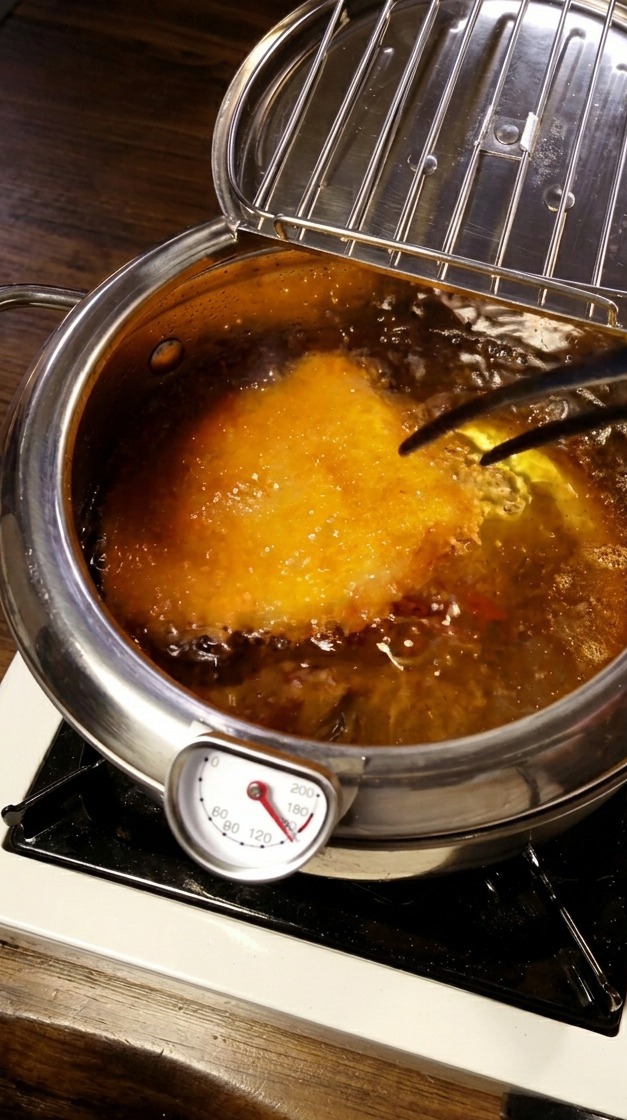 Cotoletta di maiale che frigge in olio bollente con termometro