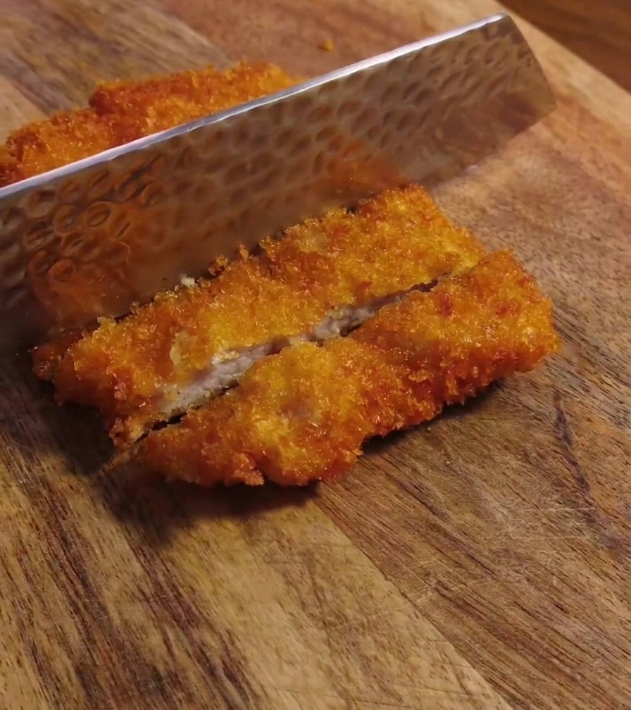 Coltello che taglia la cotoletta fritta croccante su un tagliere