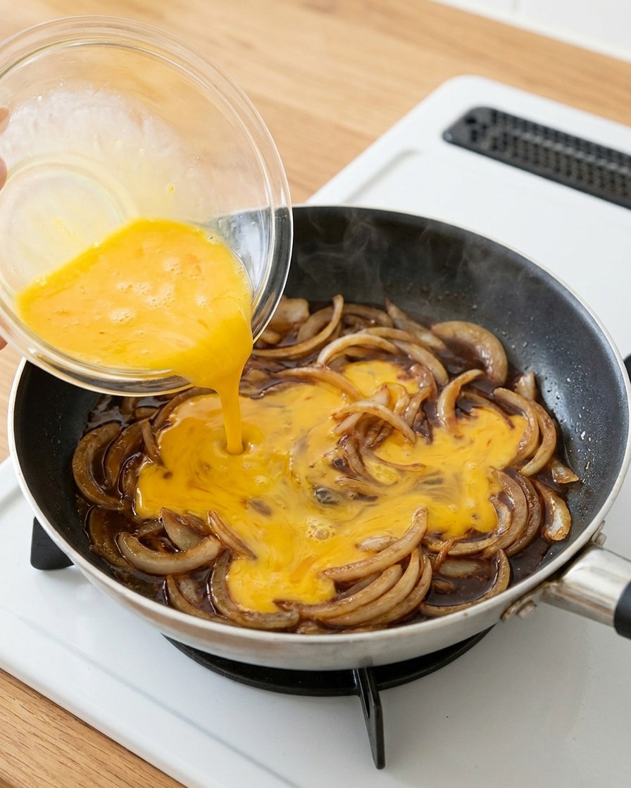 Uova sbattute versate sopra le cipolle condite in padella